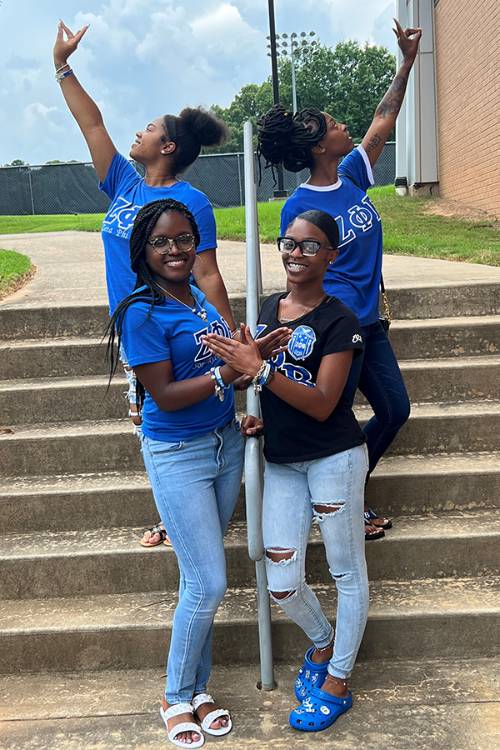 Image of four members of the Iota Sigma Chapter of Zeta Phi Beta Sorority, Inc. posing on stairs, holding up their hand signs